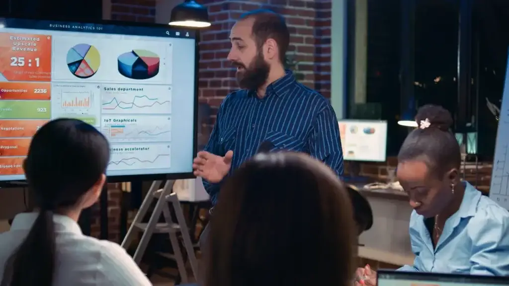 A marketing leader, perhaps a CMO defined by their role, presents business analytics on a large screen to a team.