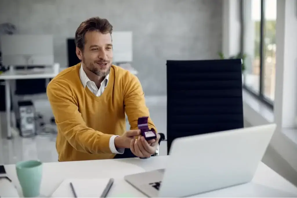 Man holding an engagement ring box during a video call, symbolizing commitment to fractional marketers.