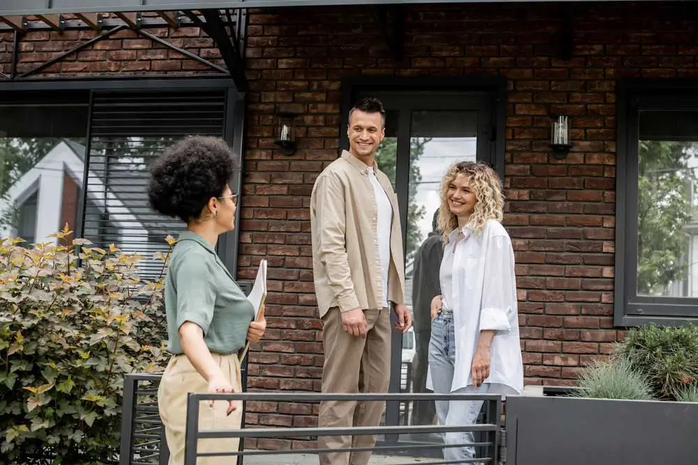 African American Real Estate Agent Talking To Smil 2023 11 27 05 32 05 Utc three people in a real estate marketing agency scenario. a confident agent with a clipboard engages with a smiling couple standing outside a modern brick house, showcasing professional and welcoming interactions in a real estate setting