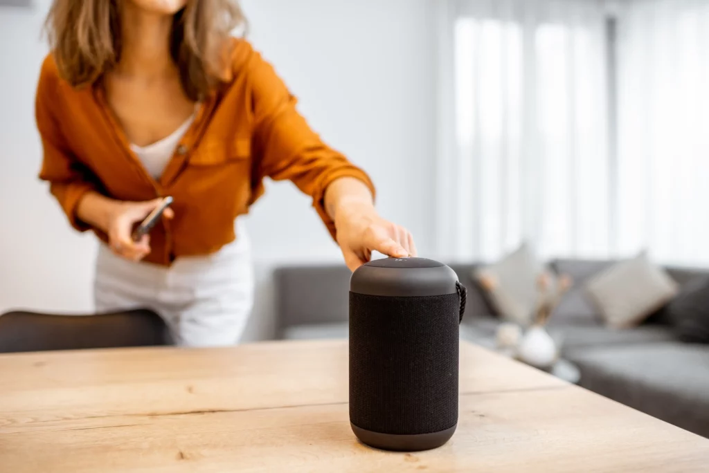 Woman in a cozy living room using a smart wireless speaker device, illustrating how everyday users interact with voice-enabled technology, emphasizing the importance of voice search local SEO for modern businesses.